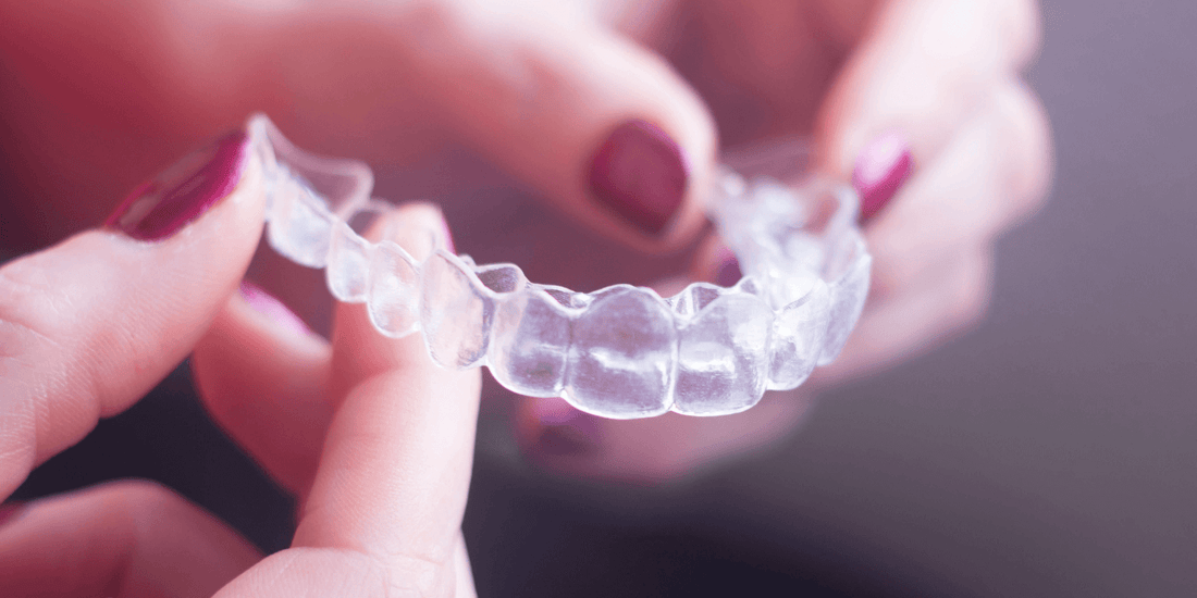woman holding clear aligner smiling listening to orthodontist