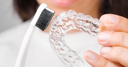 Image showing a person cleaning their clear plastic retainer with a toothbrush.